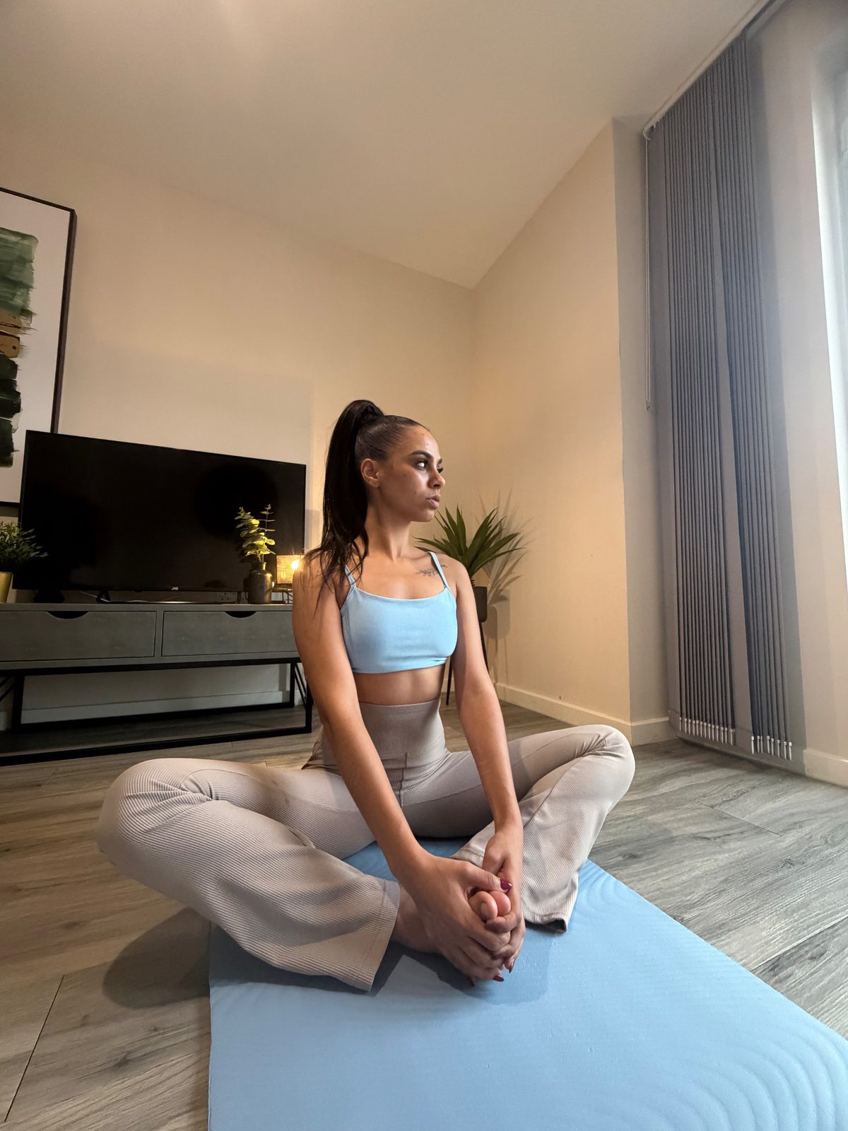 Ana in a butterfly stretch on a light blue mat in her living room