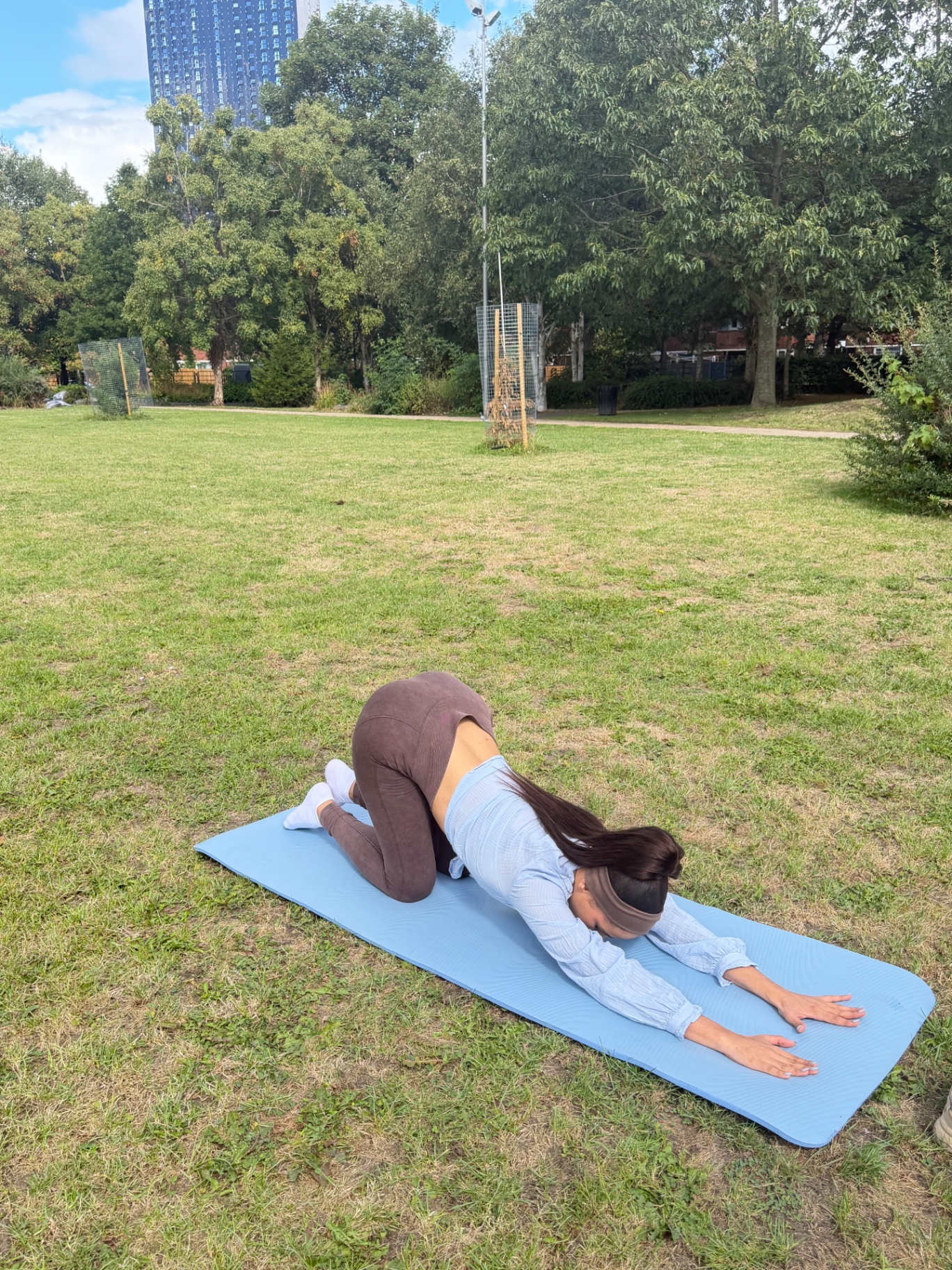 Ana in child's pose stretching on a yoga mat in the park