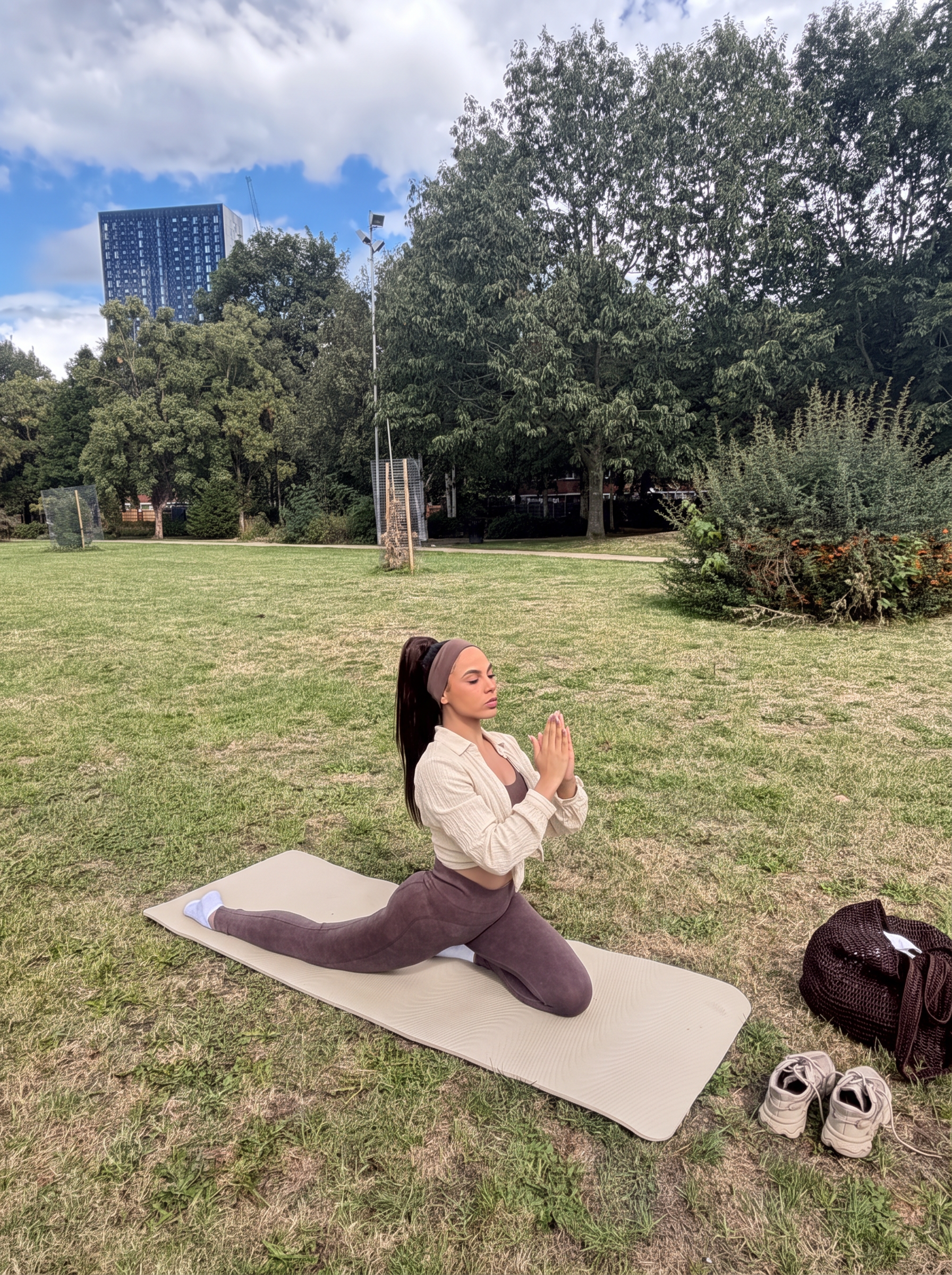 Ana in a beige shirt meditating on a beige yoga mat outdoors